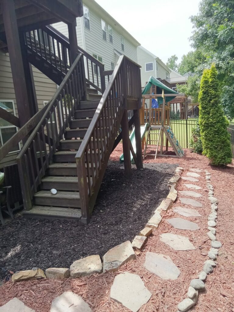 Wooden deck stairs leading to a stone path and mulched area, installed by Mels Haul & Junk Removal in Raleigh, NC.