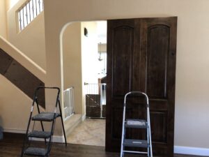 A large wooden door leaning against a wall with two step ladders, indicating a door installation or replacement project by The ABQ Handyman in Albuquerque, NM.