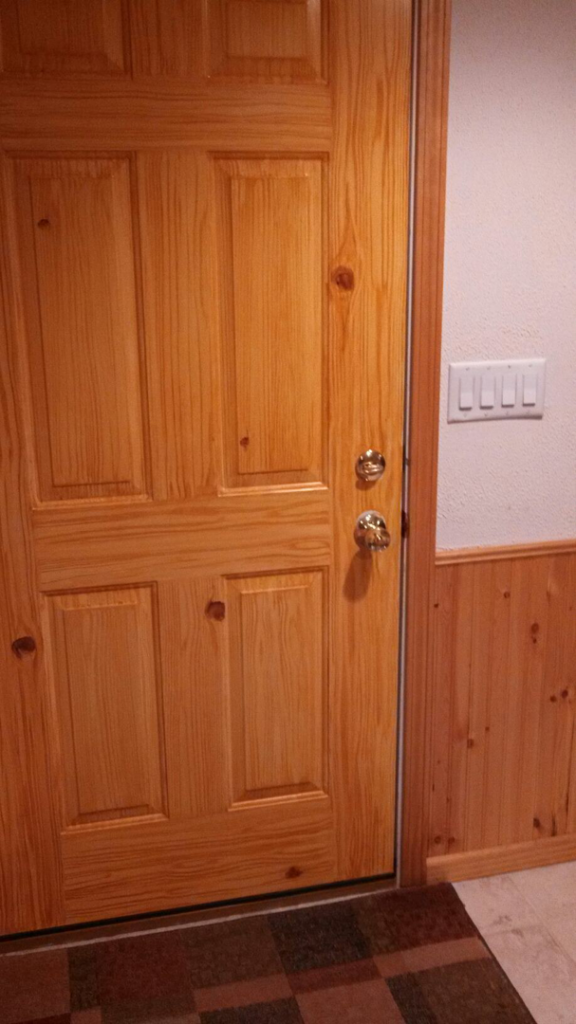 A newly installed wooden entry door with hardware and wainscoting, completed by Symphonic Painting in Oshkosh, WI.