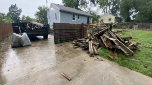 A pile of wooden fence and deck debris next to a Haul-Away Junk Removal and Dumpster Rental trailer in a backyard in Overland Park, KS.