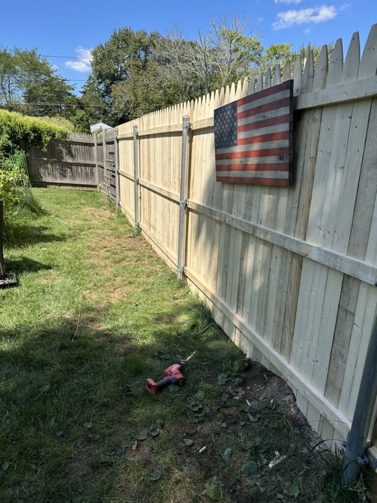 A newly installed wooden fence with a drill on the ground, showing a completed project by Woodbine Repair & Remodeling in Jamestown, RI.