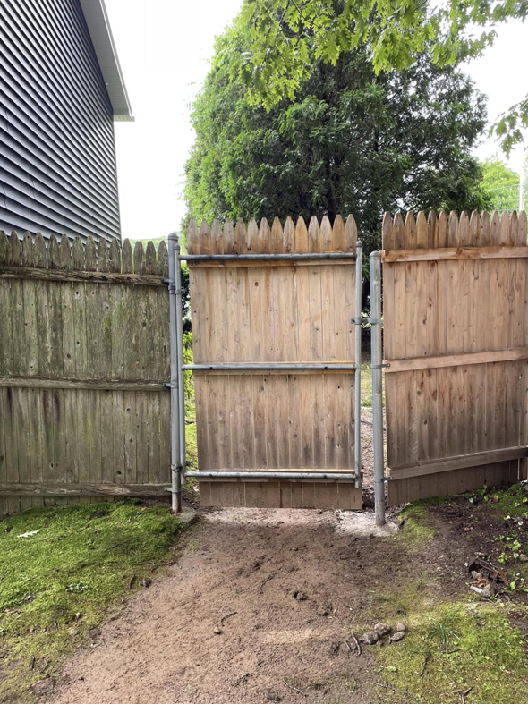 A wooden fence with a sturdy metal gate repaired by Digby Handyman Services LLC in Cranston, RI.