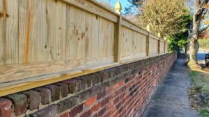 A newly installed wooden fence built on top of a brick wall along a sidewalk by Minors Fences in Ashland, VA.