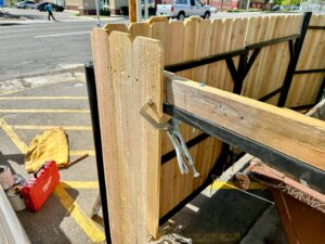A wooden fence panel being installed onto a metal frame, held by clamps, showcasing fence repair or installation by Jeremy's Welding & Handyman in West Jordan, UT.