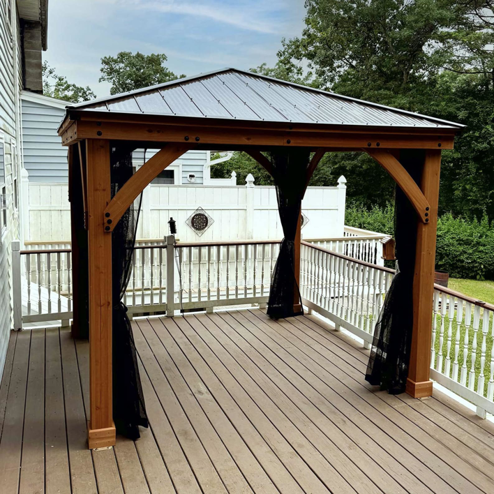 A wooden gazebo with a metal roof and curtains installed on a deck by Vlad's Handyman Services in Manchester, NH.