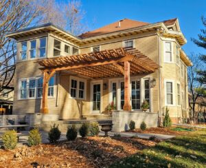 A wooden pergola extending over a patio, attached to a house, installed by Minnesota Pergolas in Lakeland, MN.