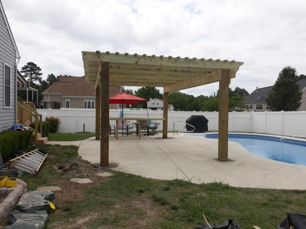 A wooden pergola providing shade over a patio and pool area by Signature Deck & Pergola in Virginia Beach, VA