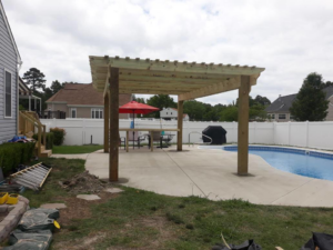 A wooden pergola providing shade over a patio and pool area by Signature Deck & Pergola in Virginia Beach, VA