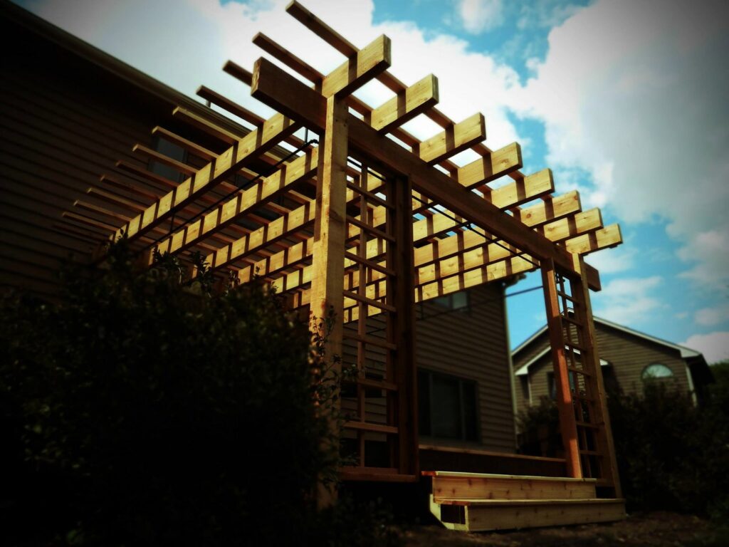 A wooden pergola structure with steps leading to a home's entrance, installed by Minnesota Pergolas in Lakeland, MN.