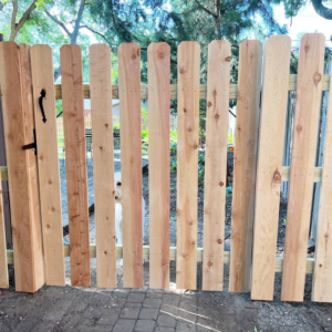 A newly installed wooden picket fence gate with a black handle by Cutting Edge Contracting and Handyman in Minneapolis, MN.