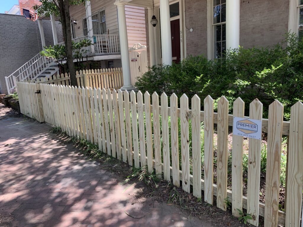 A wooden picket fence installed along a sidewalk in front of a house by Premier Fence Company in Glen Allen, VA.