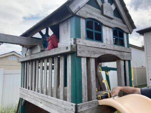 A handyman performing repairs on a wooden outdoor playset with a power drill for K-Way's Handyman Services in Lincoln, NE