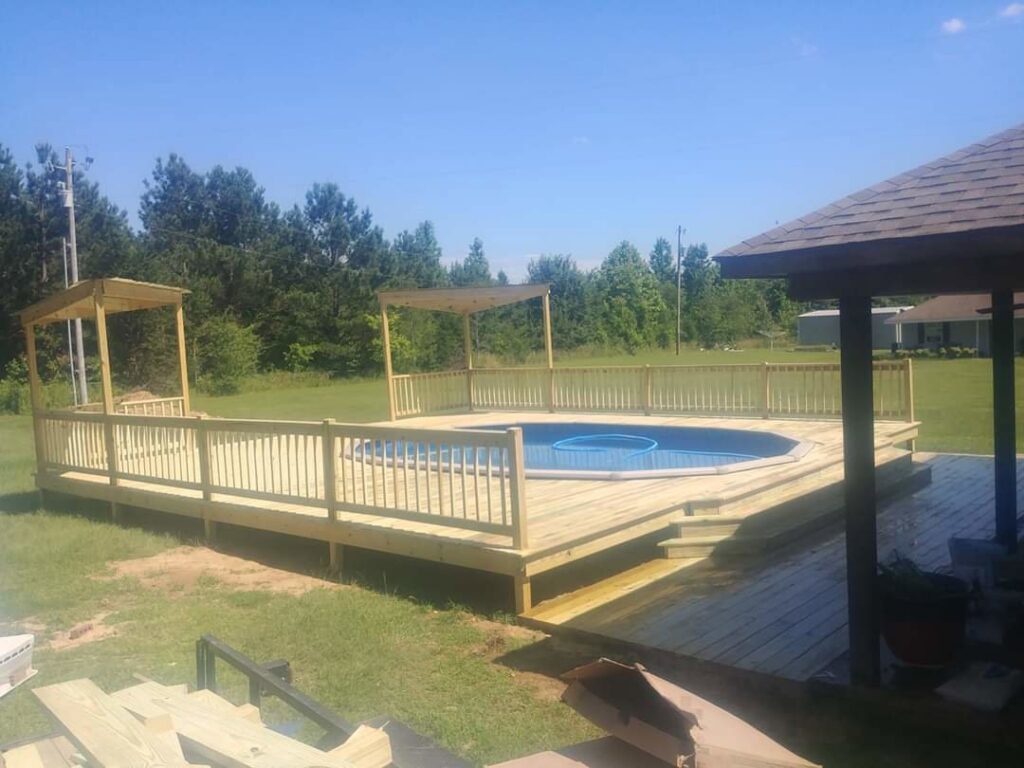 A large wooden deck with railings and pergolas built around an above-ground pool, constructed by Lee's Handyman Service LLC in Oxford, MS.