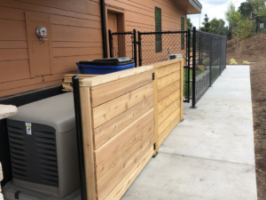 A newly installed wooden privacy fence section next to an outdoor generator by J & M Fence Co. in Vancouver, WA.