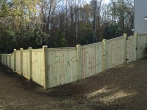 A newly installed wooden privacy fence with a gate, expertly built to follow the sloped terrain by Frontline Fencing LLC in Summerville, SC.