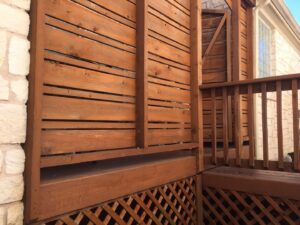 A custom-built wooden privacy screen and lattice installed next to a stone house by Savala's Remodeling Services in Austin, TX.
