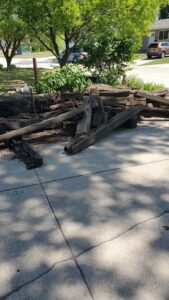A pile of heavy wooden railroad ties or timber debris on a driveway, ready for removal by KJ Haul Away Junk Removal in Cedar Rapids, IA.