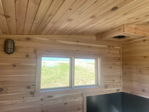 Detailed interior view of a wooden sauna ceiling, window, light fixture, and vent by No Boundaries Tiny Homes in Eau Claire, WI