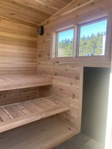 Interior of a custom wooden sauna featuring multiple tiered benches and a large window by No Boundaries Tiny Homes in Eau Claire, WI