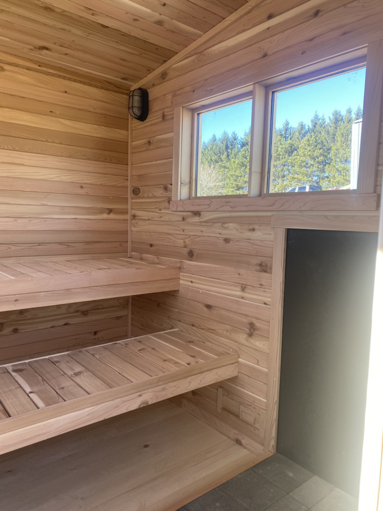 Interior of a custom wooden sauna featuring multiple tiered benches and a large window by No Boundaries Tiny Homes in Eau Claire, WI