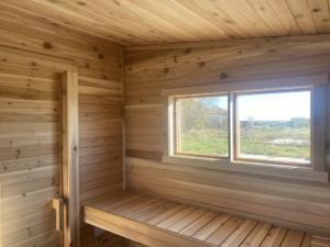 Interior view of a wooden sauna showing a large window and a sturdy wooden bench by No Boundaries Tiny Homes in Eau Claire, WI
