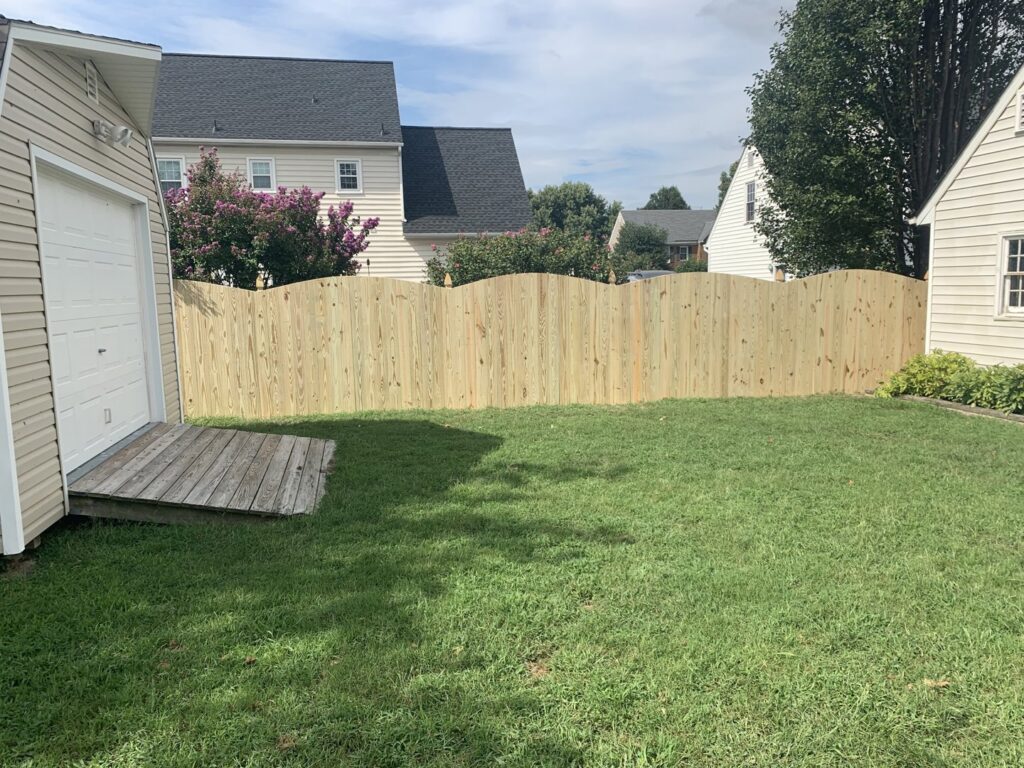 A wooden scalloped privacy fence installed in a backyard next to a garage by Premier Fence Company in Glen Allen, VA.