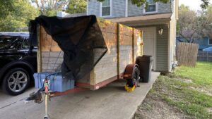A wooden-sided trailer, likely for junk removal or dumpster rental, parked in a residential driveway by Haul-Away in Overland Park, KS.