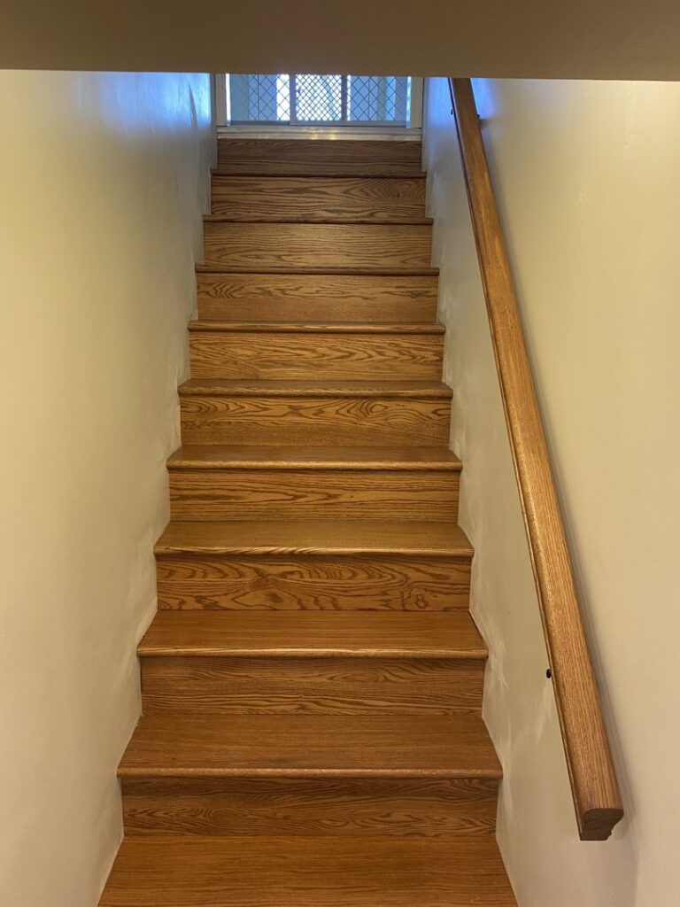 A newly installed or refinished wooden staircase with a handrail, a handyman service from Newhouse Construction St Louis in St. Louis, MO.