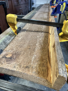 A long wooden board clamped to a workbench during a custom woodworking project by Valleys Finest Custom Finishes LLC in Salem, OR.