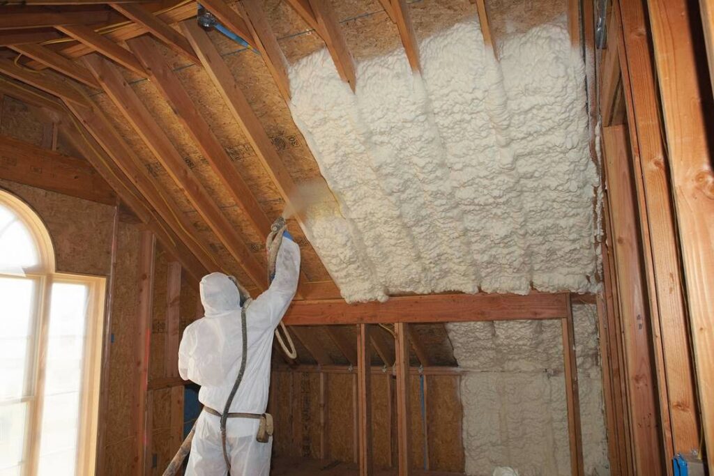 A worker in protective gear applying spray foam insulation to an attic roofline, a service by Spray Foam Solutions Of Erie in Erie, PA.