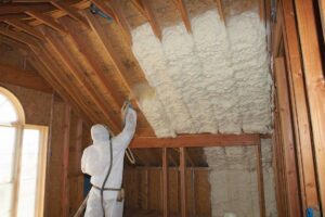 A worker in protective gear applying spray foam insulation to an attic roofline, a service by Spray Foam Solutions Of Erie in Erie, PA.