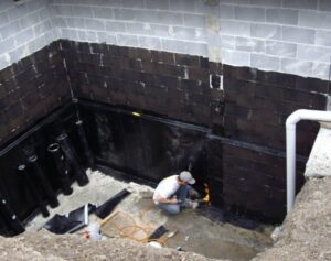 A worker applying waterproofing material to a basement wall, a service provided by Advanced Seamless Gutters, Inc. in Chicopee, MA.