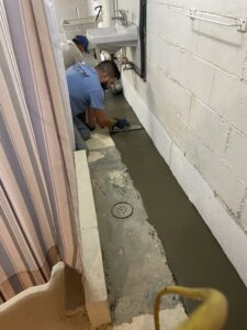 A worker from TCM Waterproofing, LLC applying concrete sealant during a basement waterproofing installation in Canton, OH.