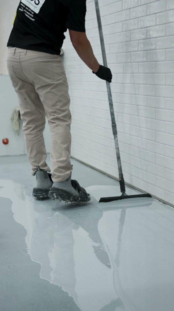 A skilled worker applying a fresh epoxy floor coating with a squeegee for Floor Coating Specialist in St. Petersburg, FL.