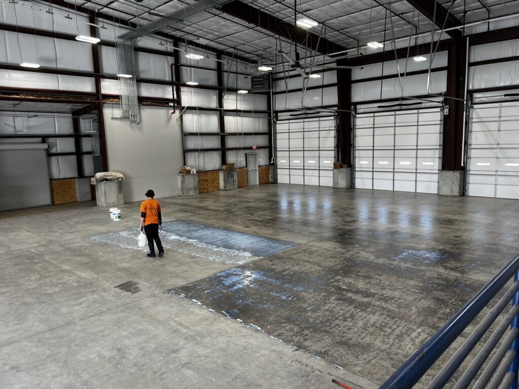A worker applying a protective coating to a large concrete floor in a commercial warehouse by Simply Construction in Las Vegas, NV.