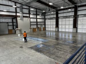 A worker applying a protective coating to a large concrete floor in a commercial warehouse by Simply Construction in Las Vegas, NV.