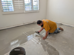 A worker applying self-leveling compound to a floor during a renovation by Prestwick Custom Homes in Gilbert, AZ
