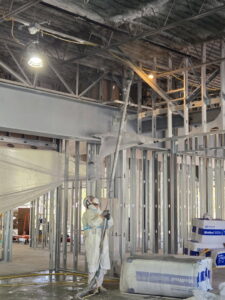 A worker applying spray fireproofing or insulation to a ceiling for Bell SPI - Shamrock Painting in Denver, CO.