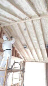 A worker applying spray foam insulation to ceiling rafters for Lantz Insulation Inc in Bird In Hand, PA.