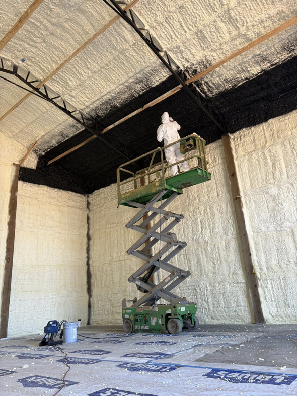 A worker on a scissor lift applying spray foam insulation to a ceiling, performed by Gulf Coast Spray Foam Insulation & Coatings, LLC in Mobile, AL