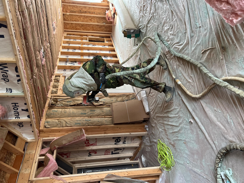 An Insulation Man worker applying spray foam insulation to a wall section near a staircase in Chesterfield, MI.