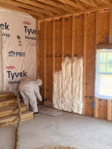 A worker in a protective suit applying spray foam insulation to wall framing for Off-Axis Spray Foam and Radon Services in Clarksville, TN.