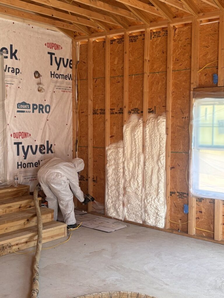 A worker in a protective suit applying spray foam insulation to wall framing for Off-Axis Spray Foam and Radon Services in Clarksville, TN.