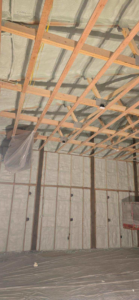 A worker on a lift applying spray foam insulation to a high wall and ceiling by Tumbarello Insulation in Peyton, CO.
