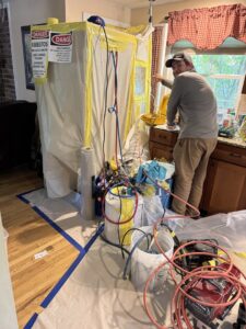 A worker performing asbestos abatement in a kitchen, surrounded by protective barriers, by Asbestos Abatement, Inc in Englewood, CO.