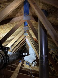 A worker in a protective suit performing mold remediation or insulation work in an attic for Pacific Insulation & Mold Remediation in Spokane, WA.