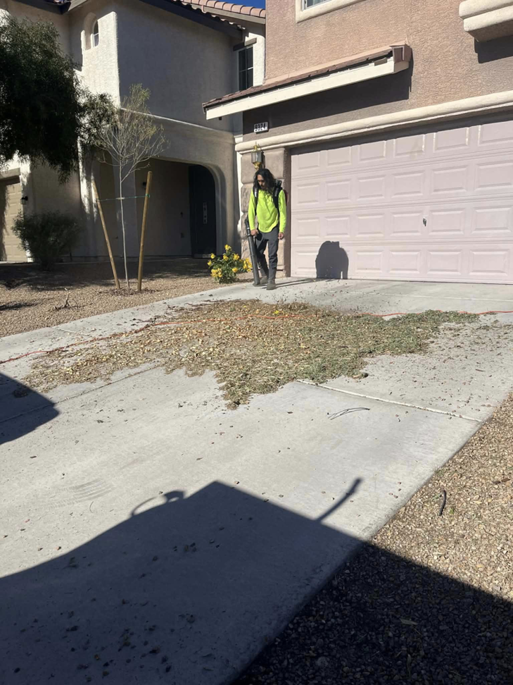A worker using a leaf blower to clear debris from a driveway for Islandscapes in North Las Vegas, NV