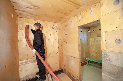A worker blowing insulation into a wall cavity during a handyman job by Custom Insulation Company, Inc. in Worcester, MA