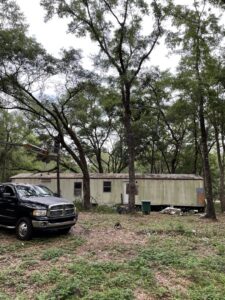 A worker in a boom lift trimming a tree next to a mobile home for Tates Tree Service in Shalimar, FL.