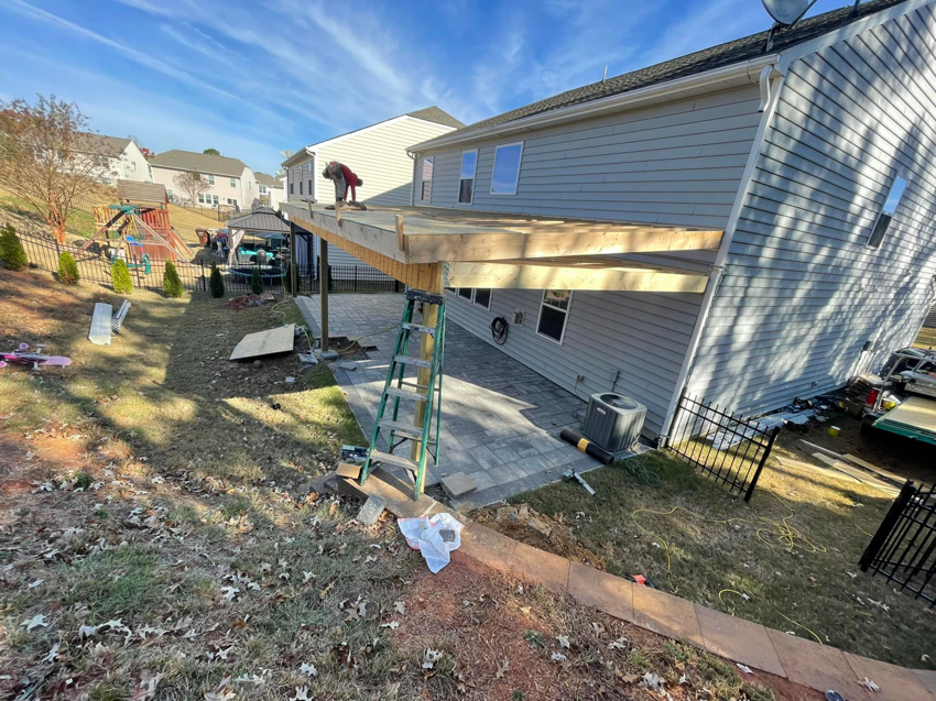 A worker on a ladder constructing a wooden patio cover for a home by A.G Deck & Painting in Charlotte, NC.